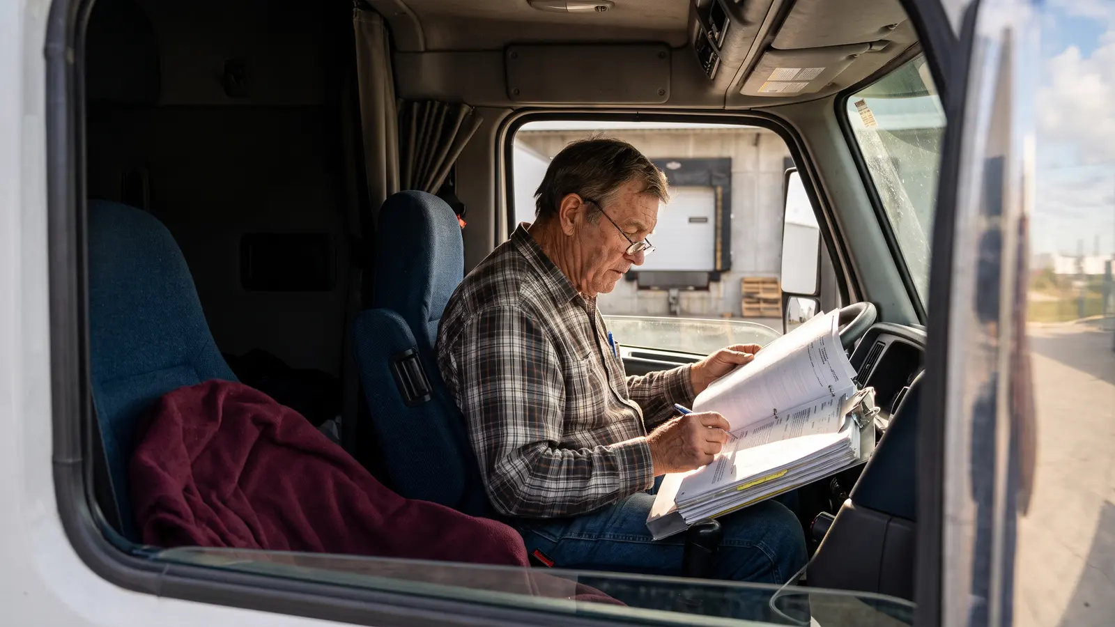 Owner-operator reading a broker-carrier agreement on a clipboard in his truck cab